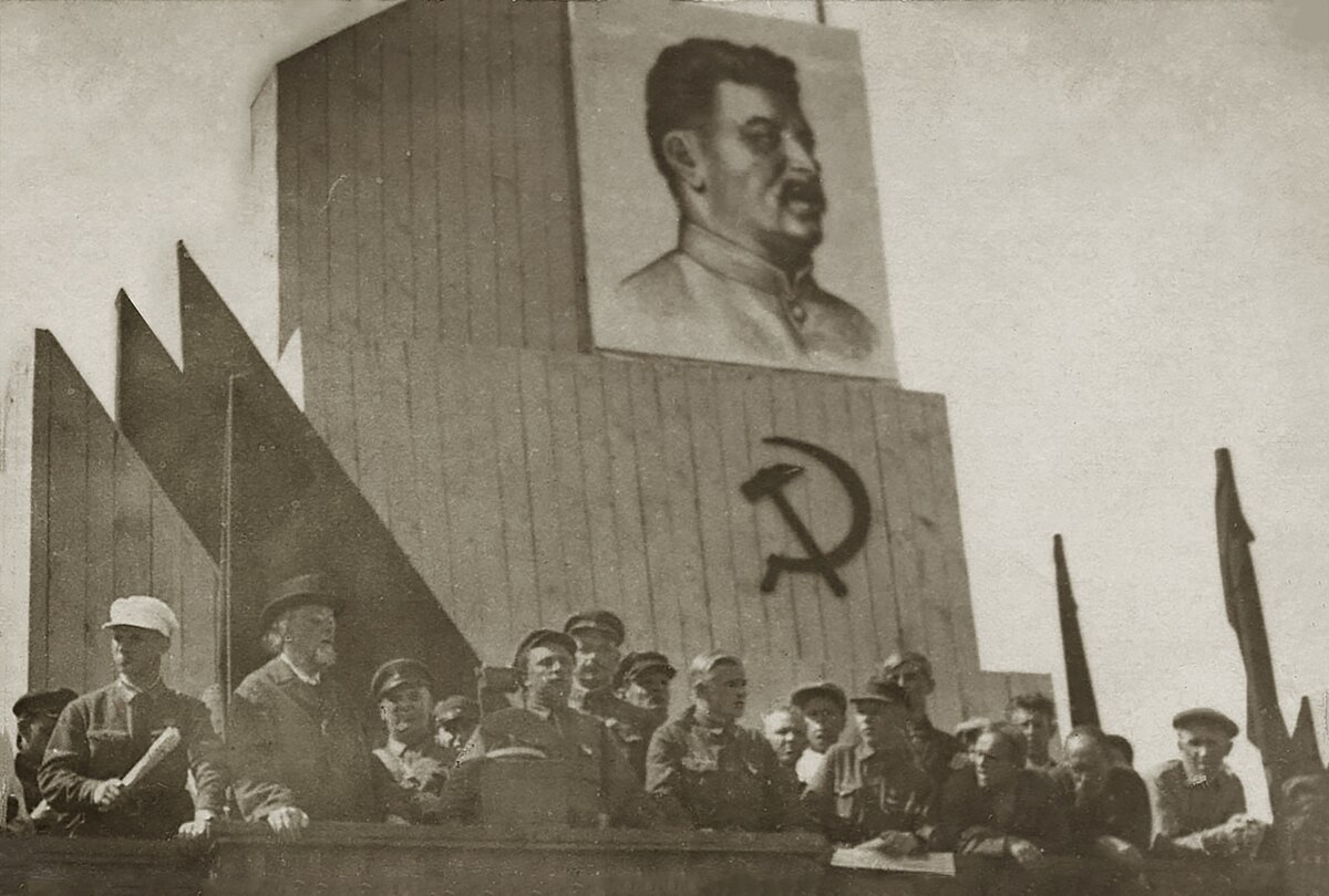 К.Э. Циолковский на трибуне среди советских и партийных работников во время районного Дня Обороны. 1934. Фотограф: Чмиль Феодосий Андроникович (1900-1945). Цифровая копия оригинальной черно-белой фотографии Константина Эдуардовича Циолковского. Источник: Wikimedia Commons (Public Domain).